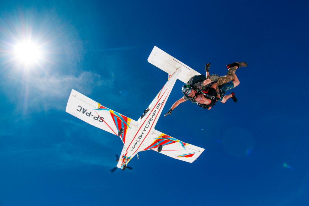 Tandem skydivers below the plane against a deep blue sky