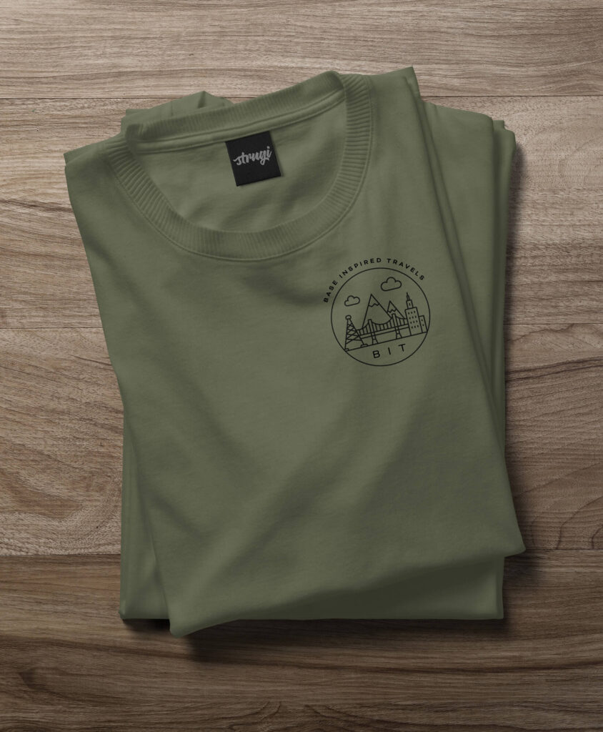 Folded olive T-shirt with a small Base Inspired Travels badge
