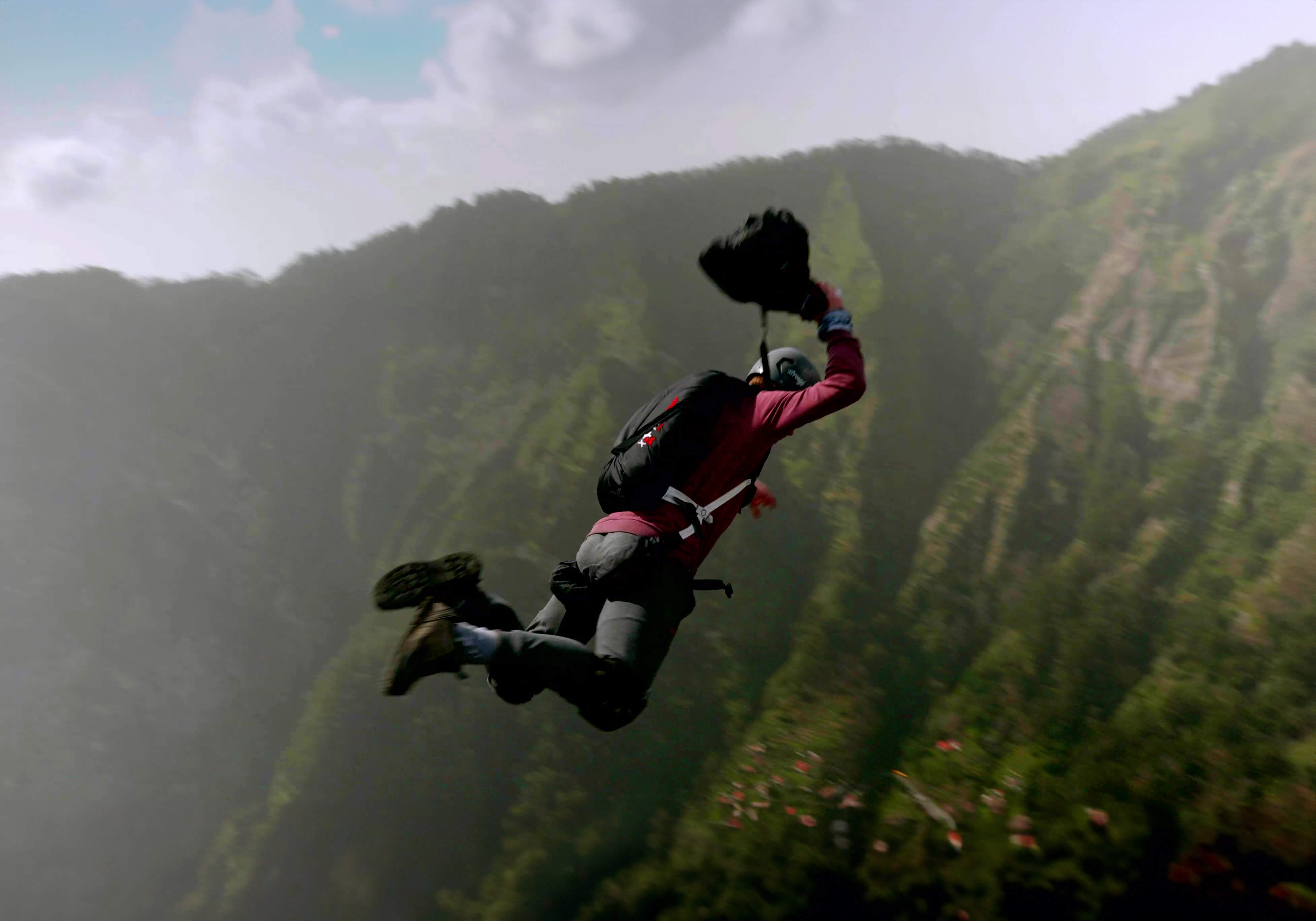 BASE jumper leaping from a misty green mountain wall