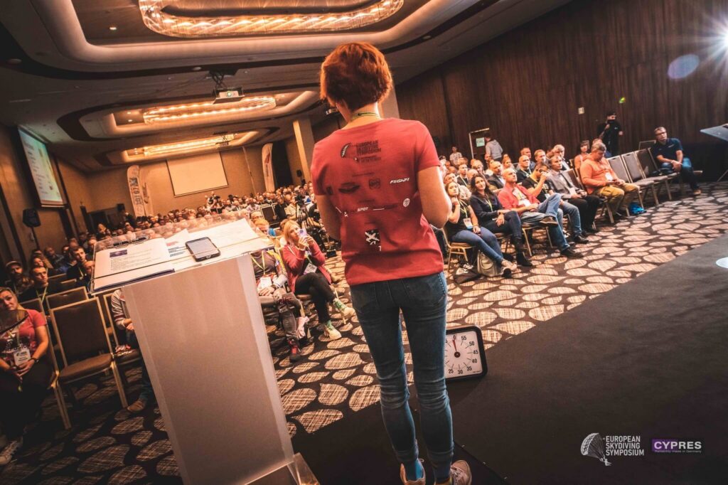 Speaker in a red T-shirt addressing the European Skydiving Symposium audience