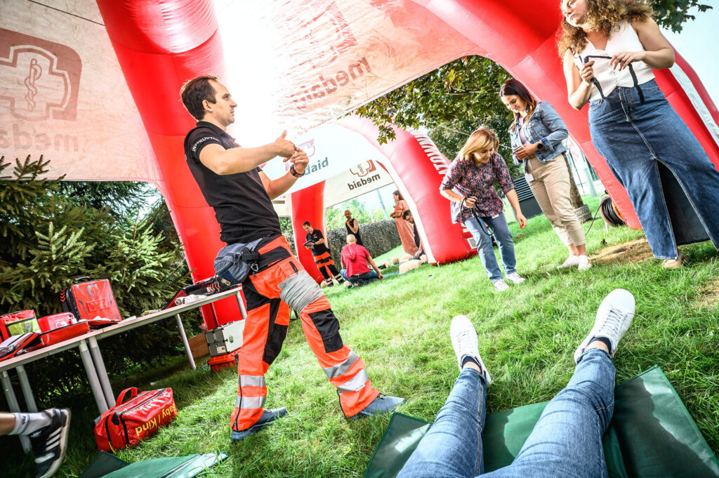 Paramedic instructor demonstrating first aid at an outdoor event under a red inflatable tent