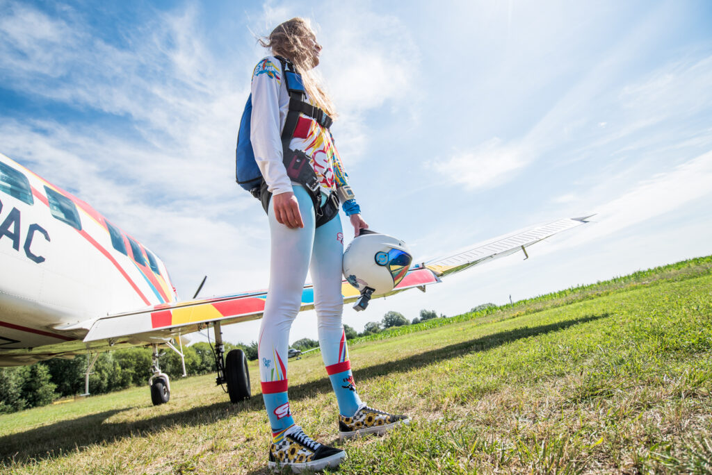 Skydiver in a colourful suit standing next to the plane on a grass airfield