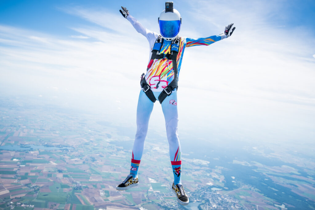 Skydiver in a colourful suit falling with arms spread, filmed from below