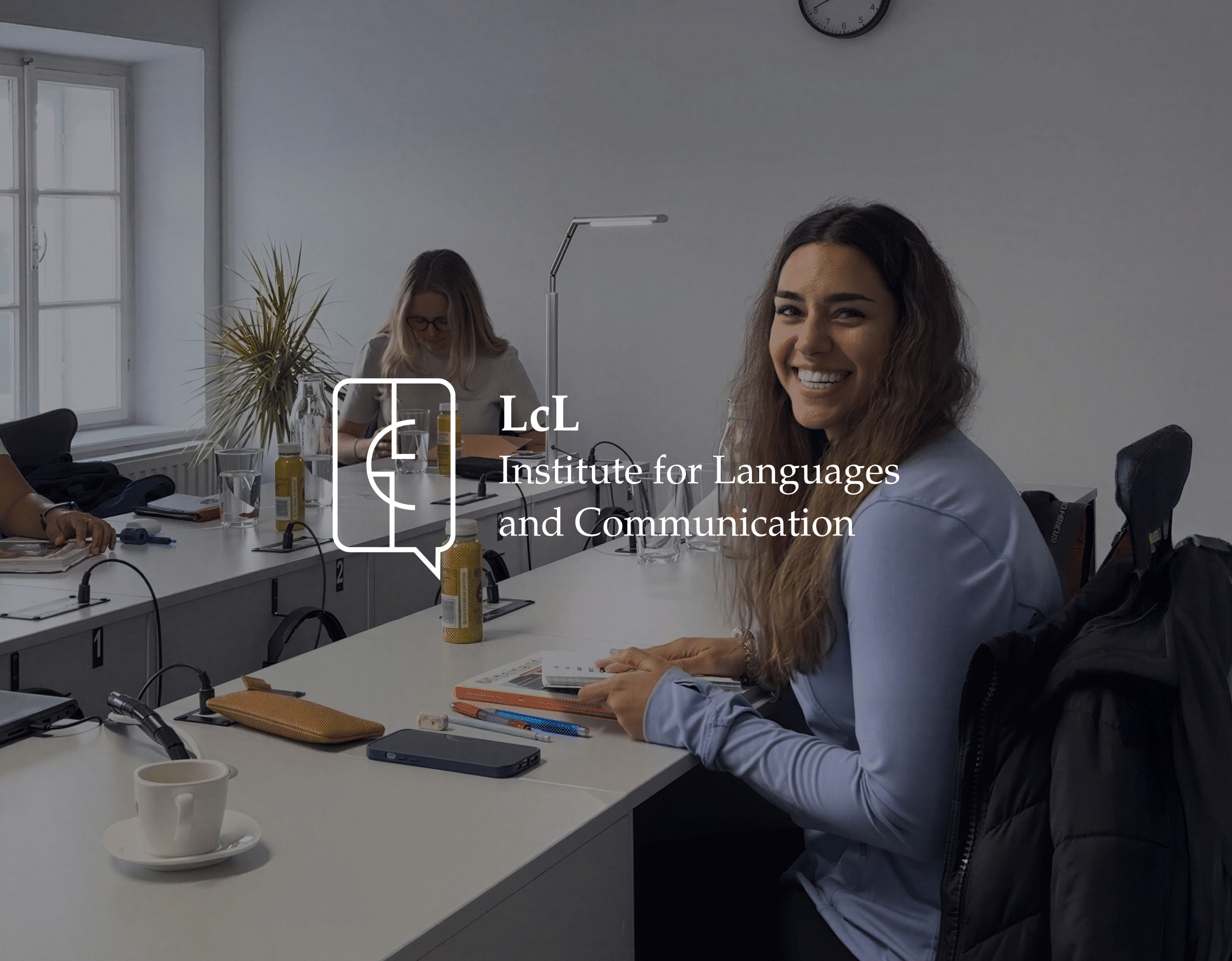Smiling woman at an office desk, with the LcL Institute for Languages and Communication logo