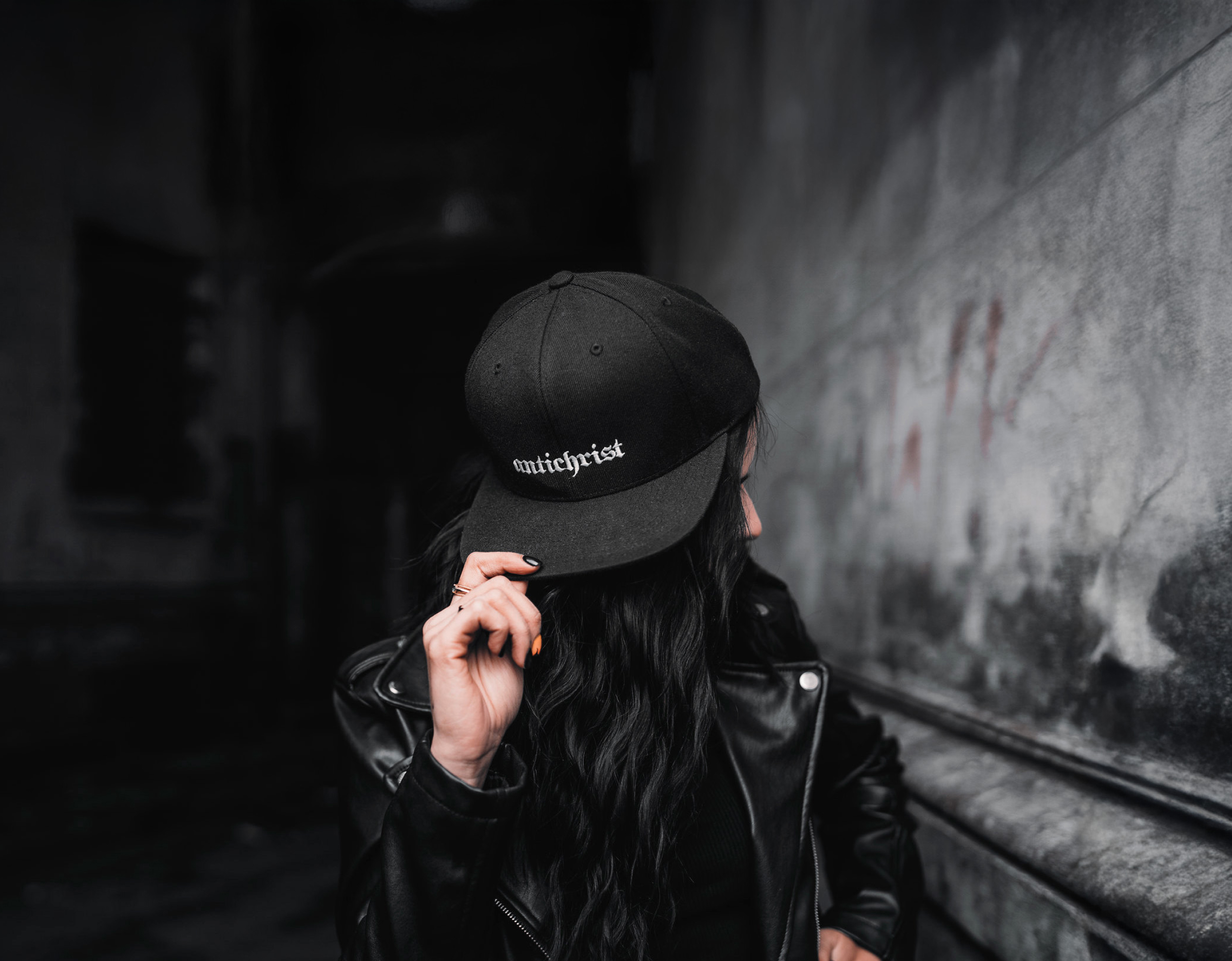 Woman in a black cap with a Holy Blvk print in a dark corridor