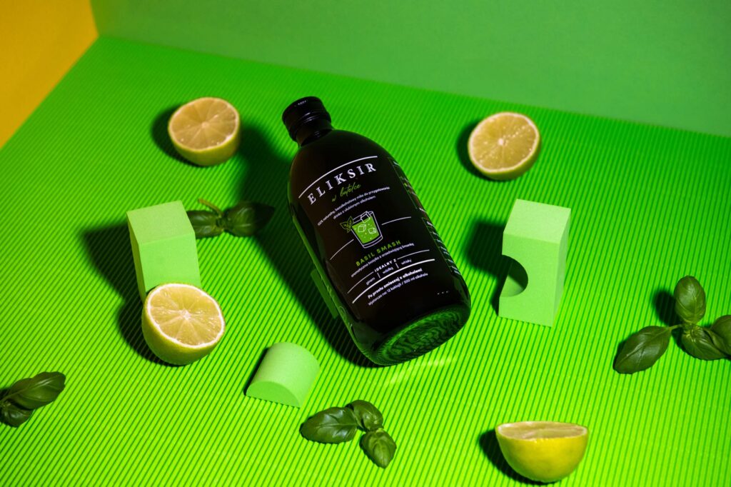 Bottle of Eliksir w butelce with limes and basil on green
