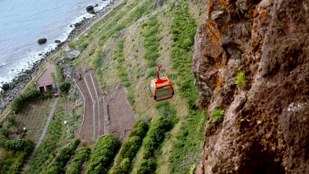 Cable car descending a steep cliff to terraced fields by the sea, Madeira