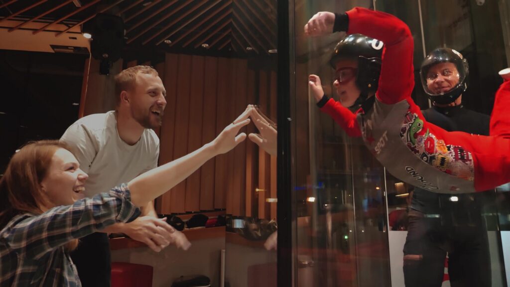 Family reaching towards the glass as a child flies in the wind tunnel