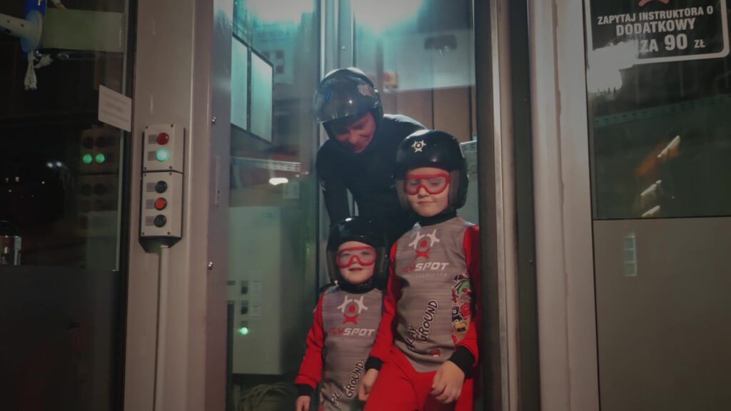 Two children in flight suits with an instructor at the wind tunnel door