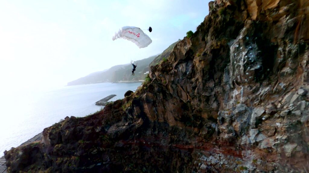 BASE jumper under canopy next to a rock face above the sea