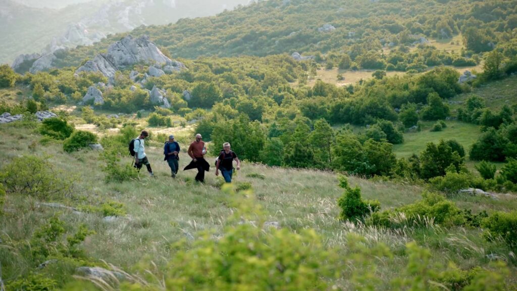 Group hiking across green hills, carrying BASE rigs