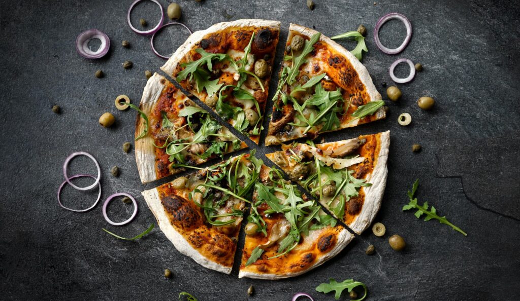Pizza with rocket and olives on a dark stone surface