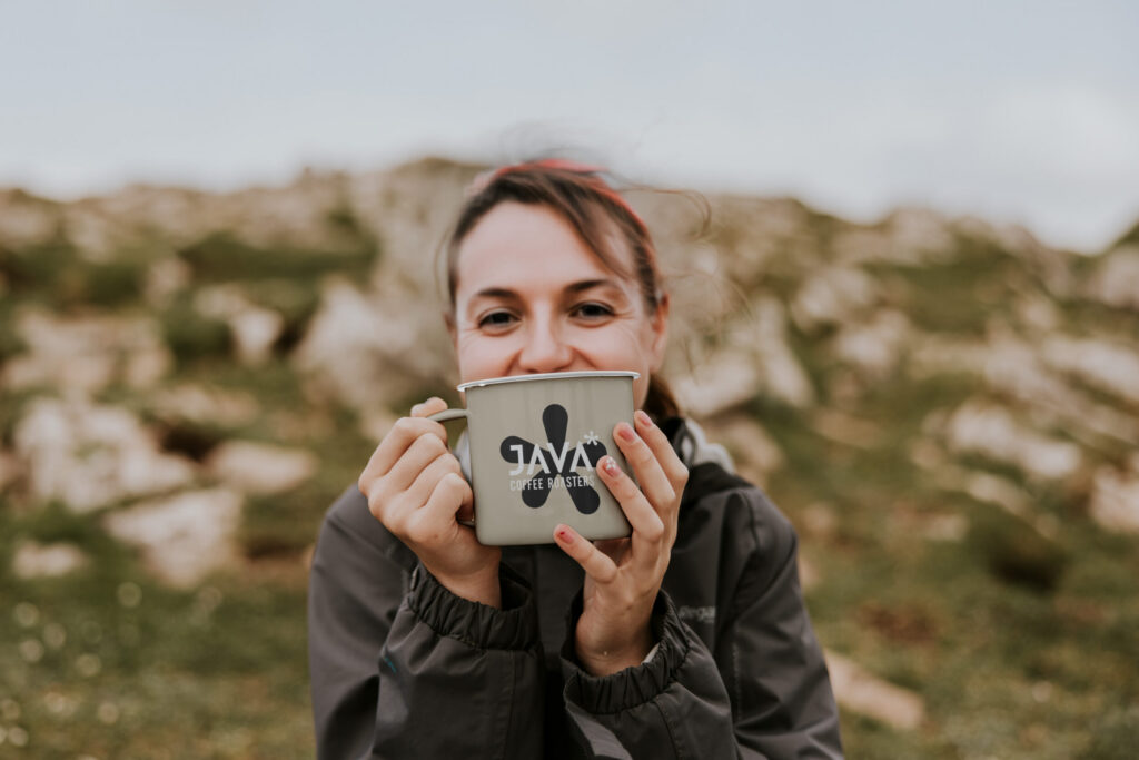 Woman drinking from a JAVA Coffee Roasters enamel mug outdoors