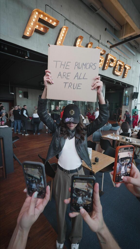 Flyspot reel still: a person holding a cardboard sign in the Flyspot lobby while others film on their phones