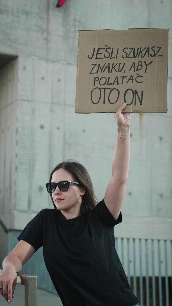 Flyspot reel still: a woman holding a sign in Polish saying this is your sign to go flying